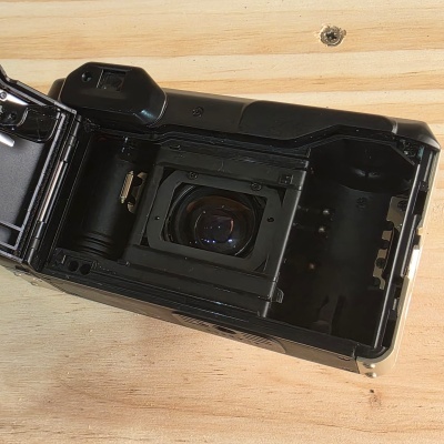 Câmara fotográfica analógica preta aberta com lente visível num suporte de madeira