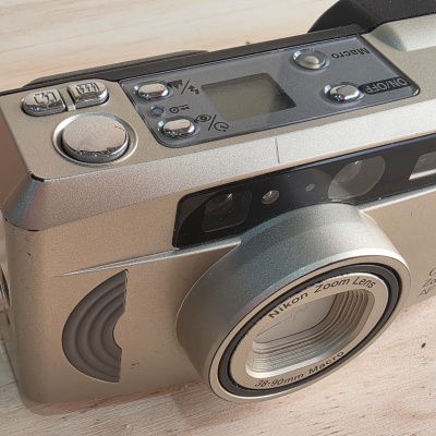 Câmara fotográfica Nikon prateada com lente zoom e botões no topo em painel prateado