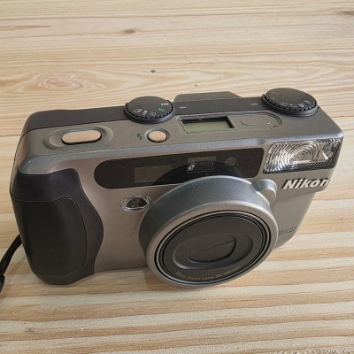 Câmara fotográfica compacta Nikon cinza metálica com detalhes pretos sobre madeira clara