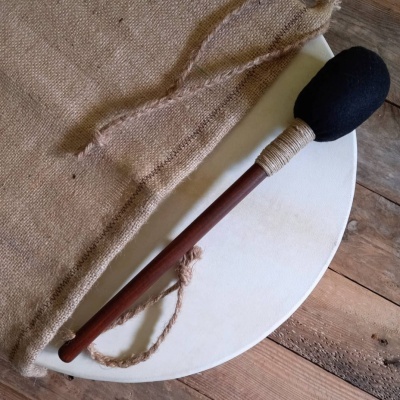 Tambor redondo branco com baqueta preta e cabo castanho sobre tecido de juta e madeira rústica