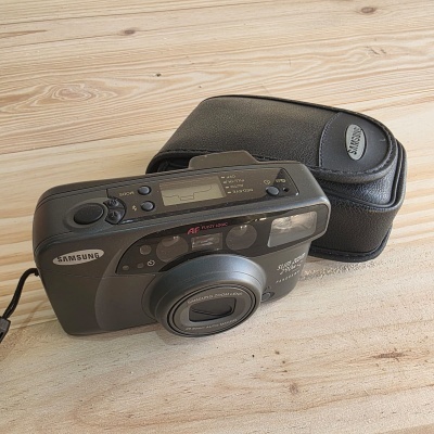 Câmara fotográfica Samsung preta com estojo preto sobre superfície de madeira clara