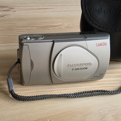 Máquina fotográfica digital Olympus prateada com correia preta sobre madeira clara