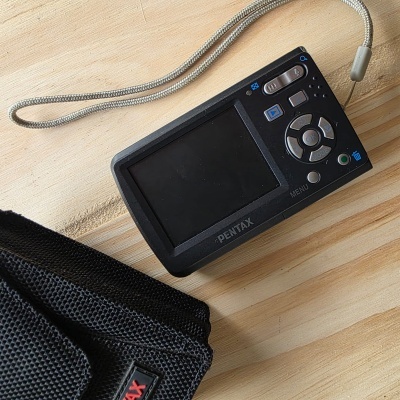 Máquina fotográfica digital preta PENTAX com ecrã LCD e bolsa preta.