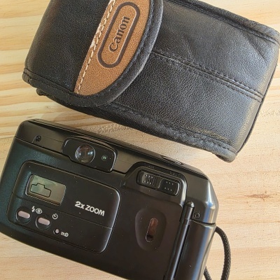 Câmara fotográfica preta com bolsa Canon em couro sobre madeira clara