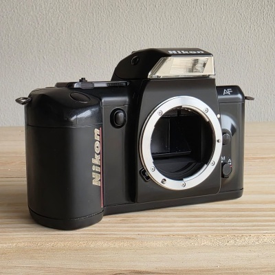 Câmara fotográfica analógica preta Nikon sem objetiva sobre mesa de madeira