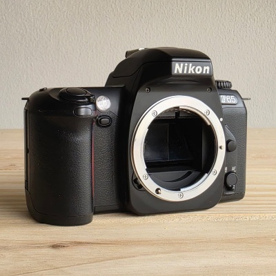 Câmara fotográfica Nikon F65 preta sem lente sobre mesa de madeira