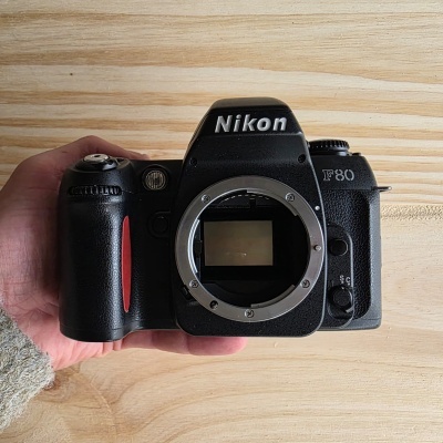 Câmara fotográfica Nikon F80 preta com detalhe vermelho e punho em madeira clara