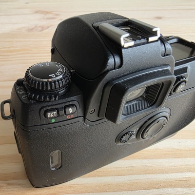 Máquina fotográfica preta de filme com botões e visor colocada sobre madeira clara