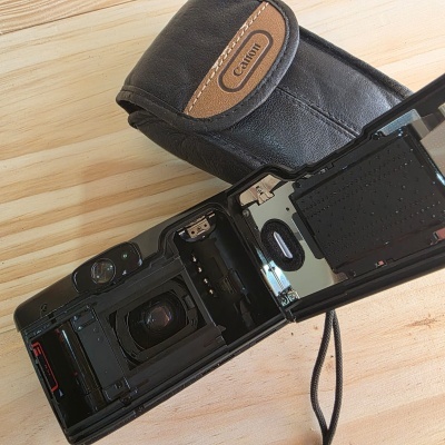 Câmara fotográfica analógica preta aberta com bolsa de couro preto sobre madeira clara