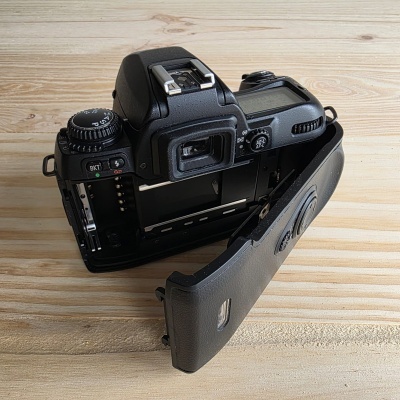 Máquina fotográfica analógica preta com visor traseiro aberto sobre madeira clara