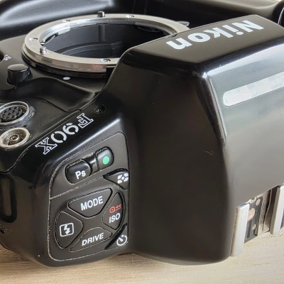 Câmara fotográfica Nikon F90X preto, sem objectiva, botões de controlo visíveis, deitada sobre superfície de madeira.