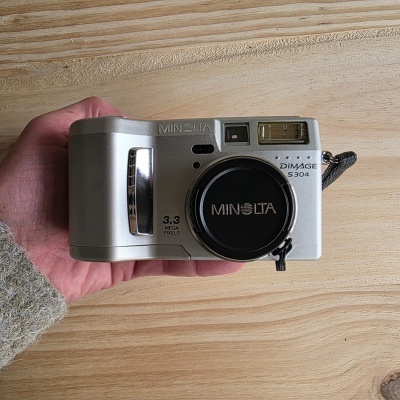 Câmara digital Minolta prateada com tampa na lente em fundo de madeira