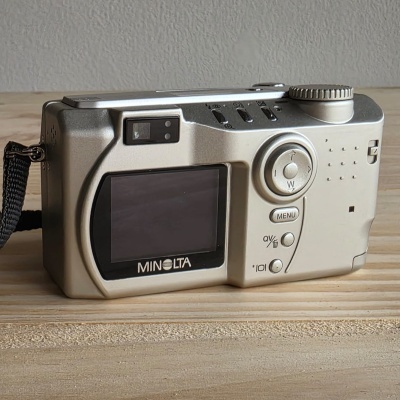 Máquina fotográfica digital Minolta cinza prateada com ecrã LCD e botões