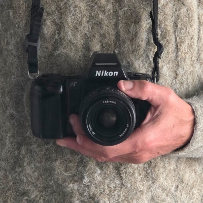 Máquina fotográfica Nikon preta com objetivo 28-70mm numa mão sobre tecido cinzento.