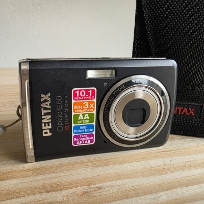 Câmara digital Pentax preta com etiquetas coloridas e bolsa preta ao fundo