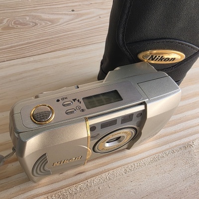 Máquina fotográfica compacta Nikon prateada com detalhes dourados e estojo preto