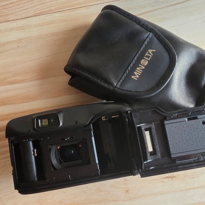 Câmara Minolta analógica preta aberta e capa de couro preta com logo Minolta.
