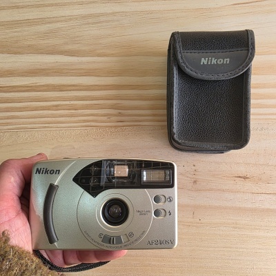 Câmara fotográfica compacta cinzenta Nikon e estojo preto sobre madeira clara