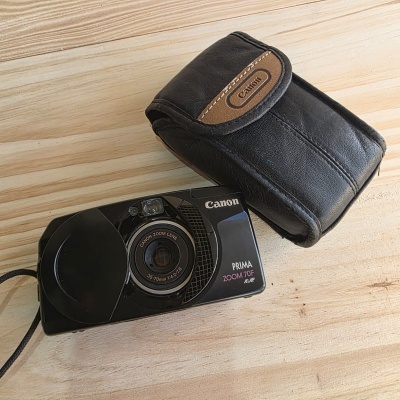 Câmara Canon PRIMA ZOOM 70F preta com estojo de pele preto em madeira clara