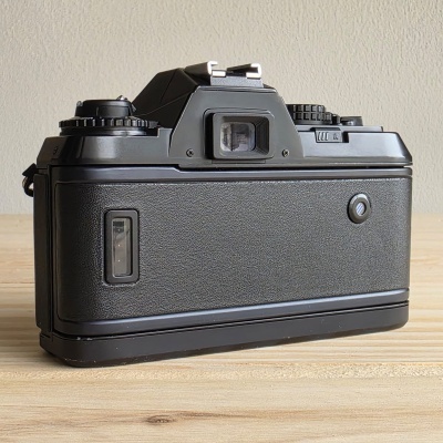Máquina fotográfica analógica preta com textura de couro na parte traseira.