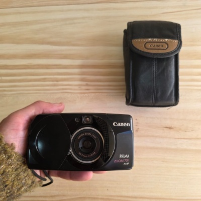 Câmara fotográfica Canon Prima Zoom 70F AiAF preta com estojo preto em superfície de madeira clara