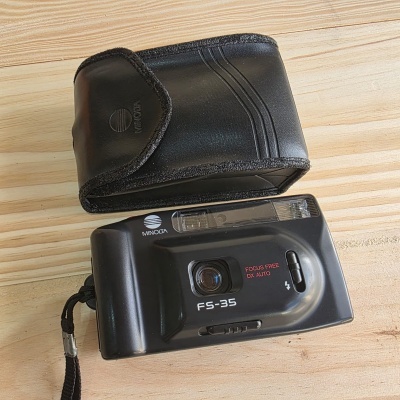 Câmara fotográfica Minolta FS-35 preta com bolsa preta sobre mesa de madeira