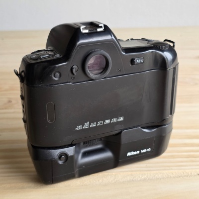 Máquina fotográfica Nikon preta com base MB-10 sobre mesa de madeira