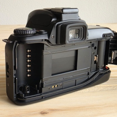 Câmara fotográfica analógica preta com parte traseira aberta sobre madeira clara