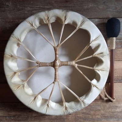 Tambor tradicional de pele branca com amarrações internas e baqueta com ponta preta num fundo de madeira