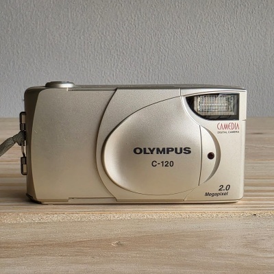 Câmara digital Olympus C-120 beje com flash sobre madeira