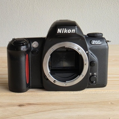 Câmara fotográfica Nikon F65 preta numa superfície de madeira clara