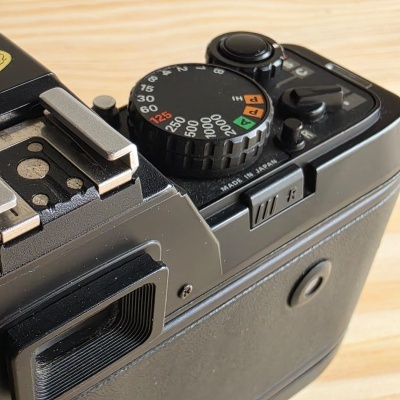 Câmara fotográfica preta com mostradores e botões de ajuste sobre mesa de madeira clara