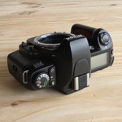 Câmara fotográfica preta Nikon F65 sobre fundo de madeira clara