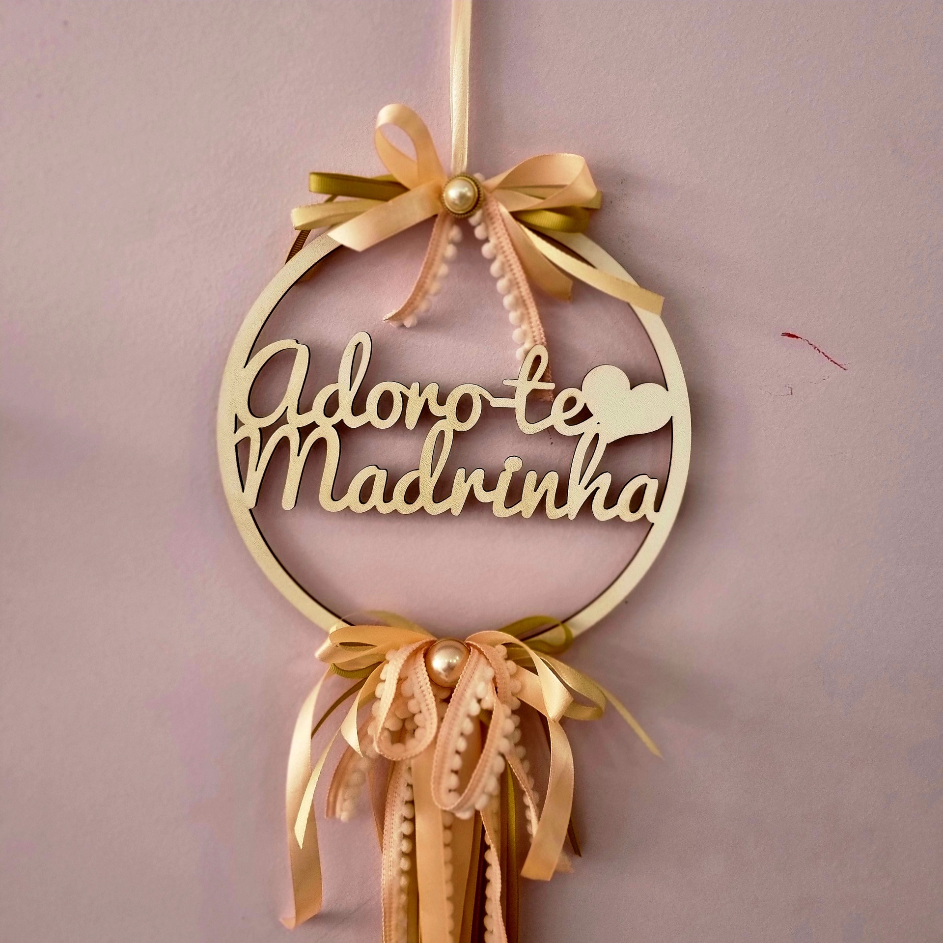 Adorno redondo em madeira com texto 'Adoro-te Madrinha' e fitas cor de rosa e dourado