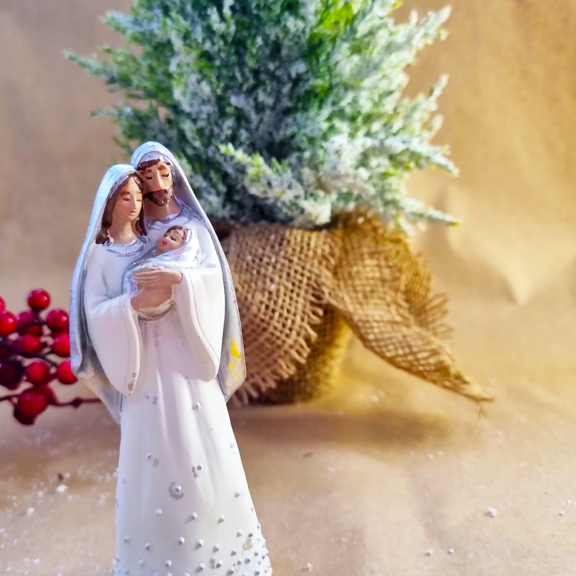 Estatueta da Sagrada Família em branco com detalhes decorativos e plantas artificiais ao fundo