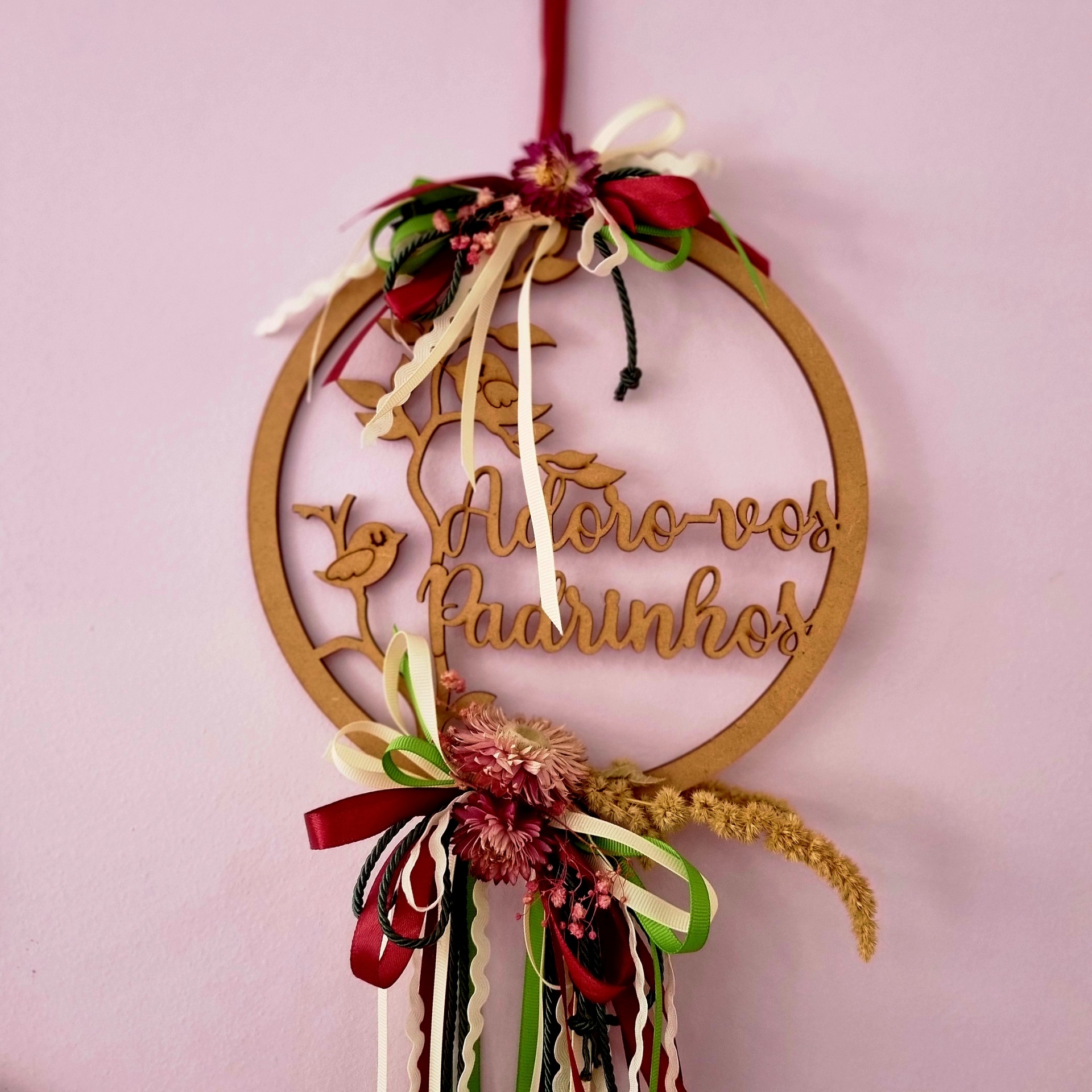 Enfeite pendurado redondo em madeira com texto e detalhes florais e fitas coloridas