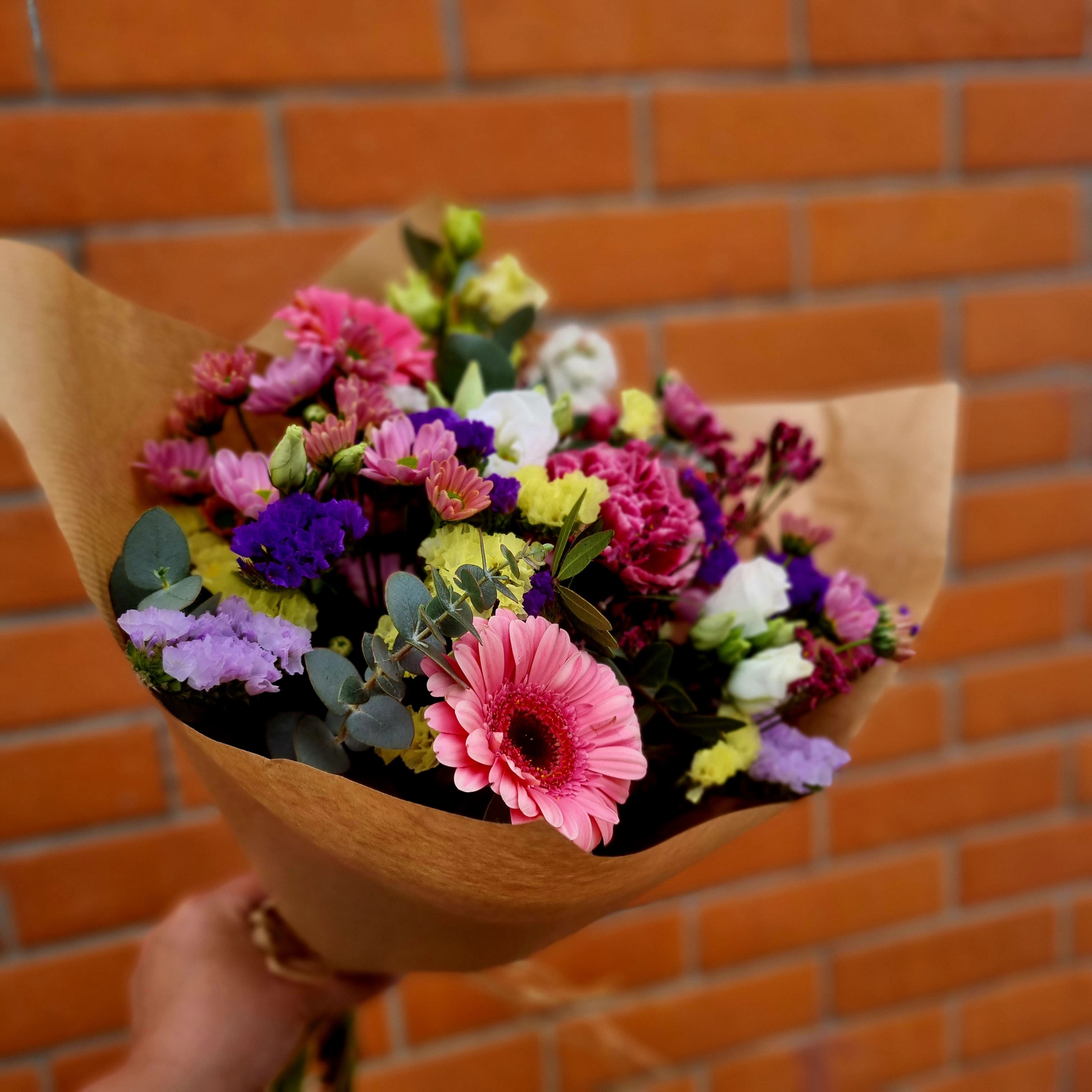 Buquê de flores coloridas em papel kraft com fundo de parede de tijolos.