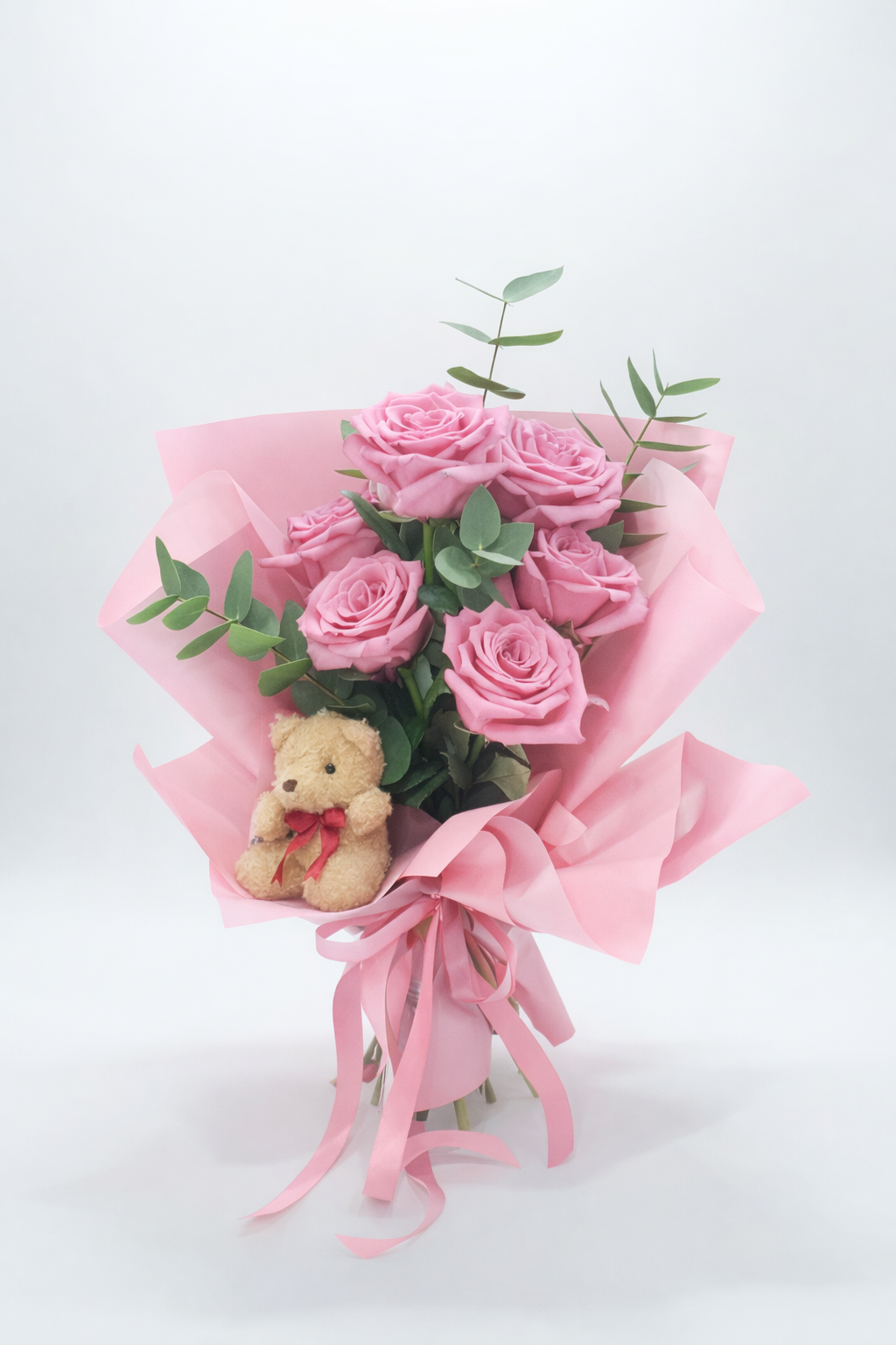 Buquê de rosas cor-de-rosa com papel e fitas cor-de-rosa e ursinho de pelúcia.