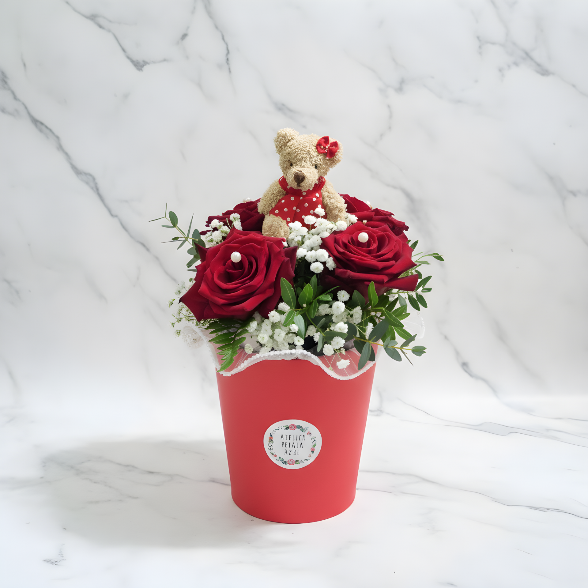 Arranjo floral com rosas vermelhas, flores brancas e urso de peluche num recipiente vermelho
