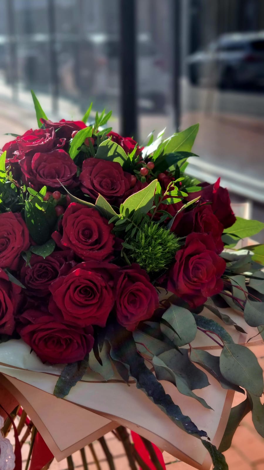 Buquê de rosas vermelhas com folhas verdes e frutos pequenos, em papel de embrulho