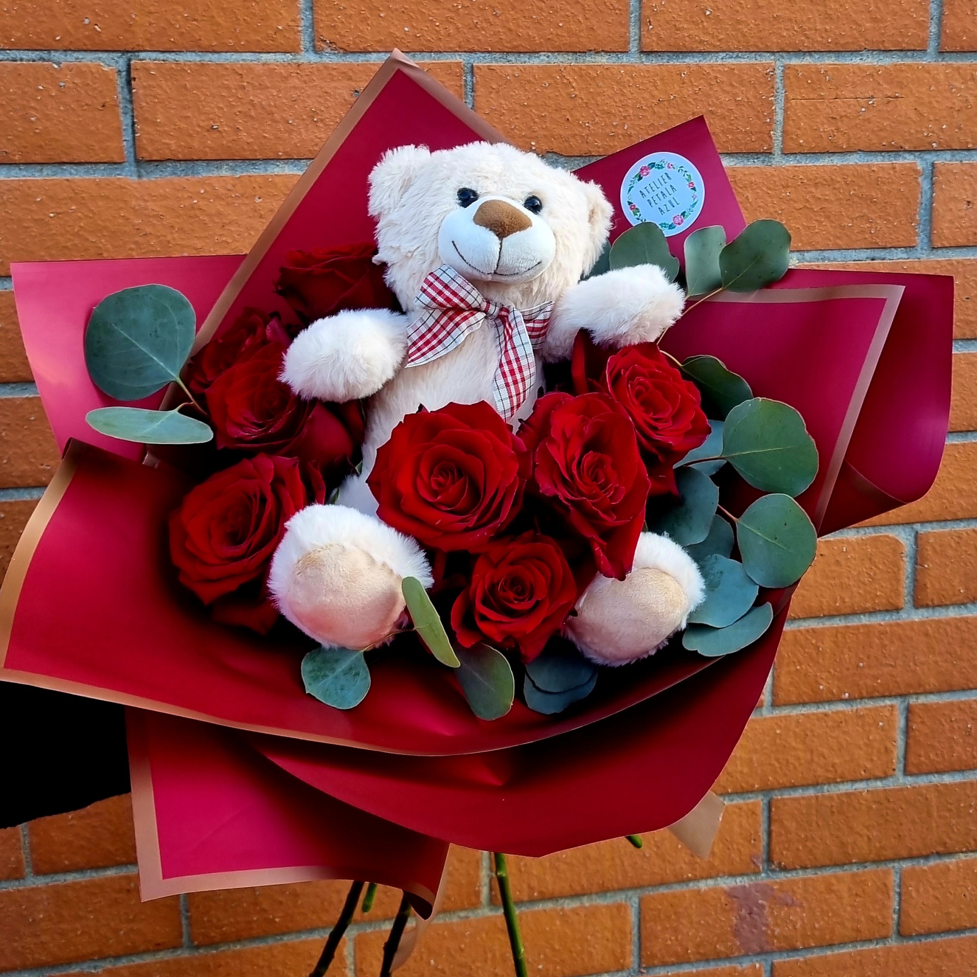 Buquê com rosas vermelhas, folhas verdes e ursinho de pelúcia branco com laço xadrez