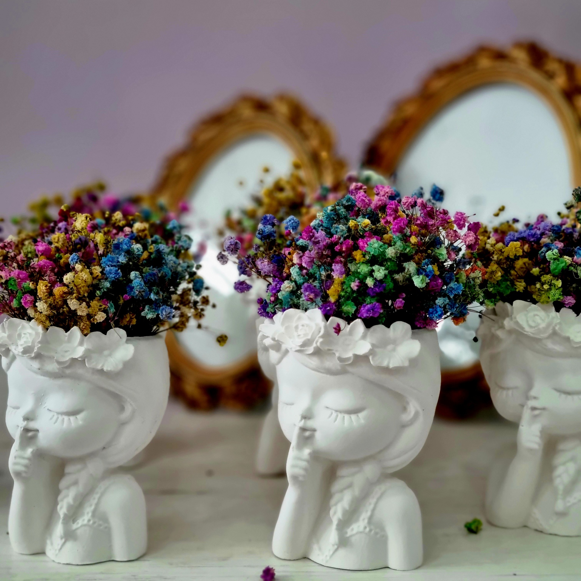 Três vasos brancos de cerâmica com flores coloridas e espelhos dourados ao fundo