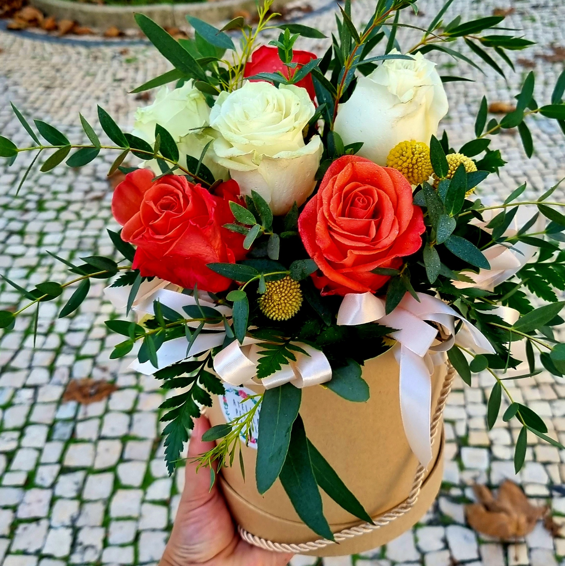 Bouquet de rosas vermelhas e brancas com folhas verdes numa caixa castanha com fita branca