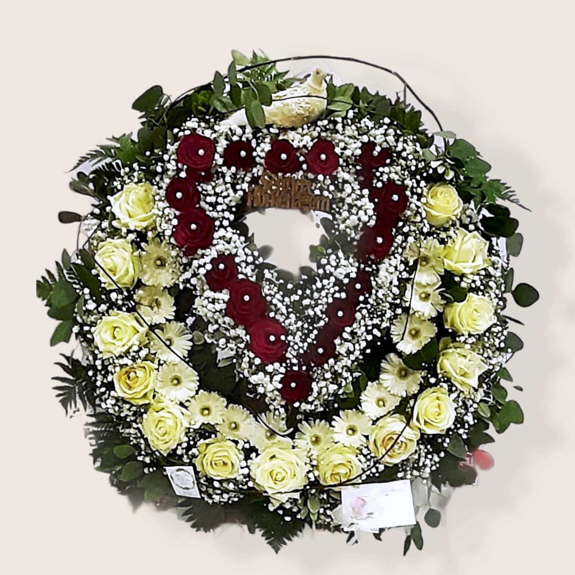 Coroa funerária em forma de coração com rosas vermelhas, flores brancas e amarelas e folhagem verde