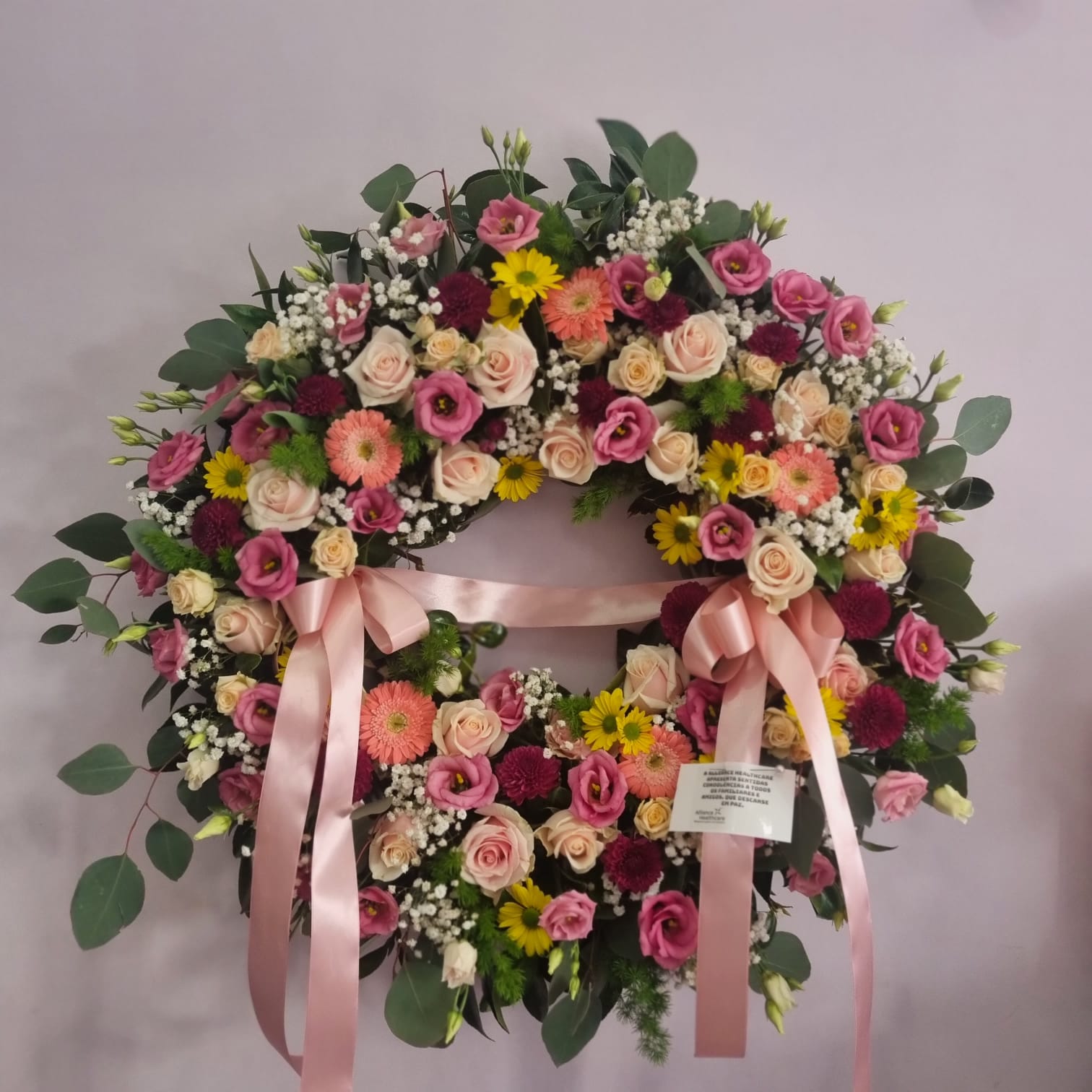 Coroa funerária colorida com rosas, lisianthus e fitas cor-de-rosa