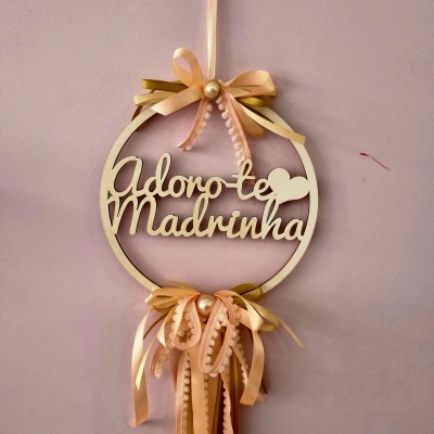 Adorno redondo em madeira com texto 'Adoro-te Madrinha' e fitas cor de rosa e dourado