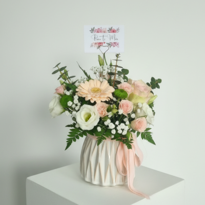 Arranjo floral com flores em vasos cerâmicos brancos e cartão decorativo.