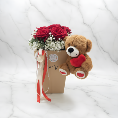 Arranjo floral com rosas vermelhas, flores brancas, caixa bege com laços e ursinho de peluche castanho com coração vermelho