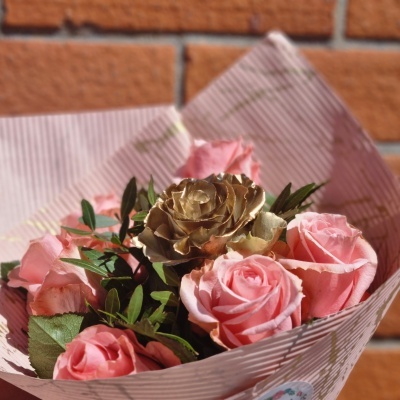 Bouquet de rosas cor-de-rosa com uma rosa dourada, folhas verdes e papel riscado dourado