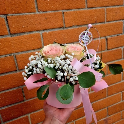 Arranjo floral com rosas, pequenas flores brancas e folhas em vaso rosa com laço